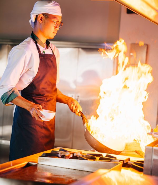 Chef hands with wok and fire. Closeup of chef cooking food with flames in professional kitchen. Expertise at work busy cooking handling flames in a modern setting. cook food with fire