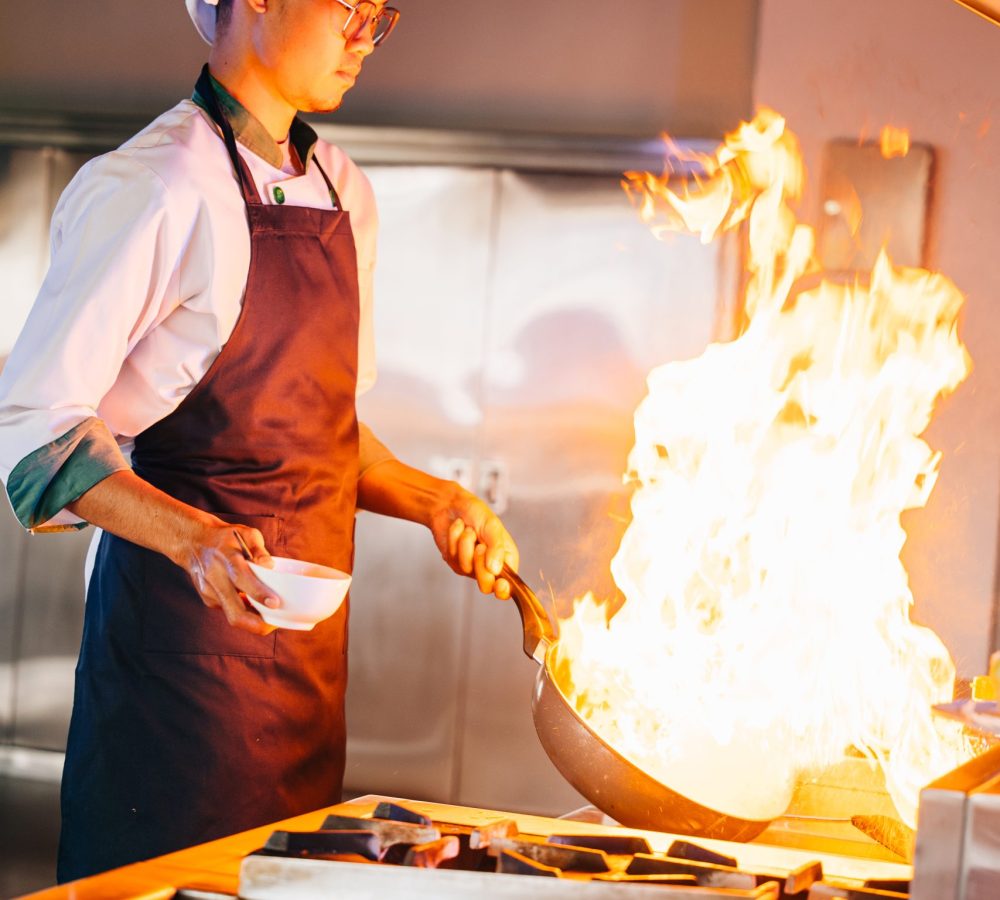 Chef hands with wok and fire. Closeup of chef cooking food with flames in professional kitchen. Expertise at work busy cooking handling flames in a modern setting. cook food with fire