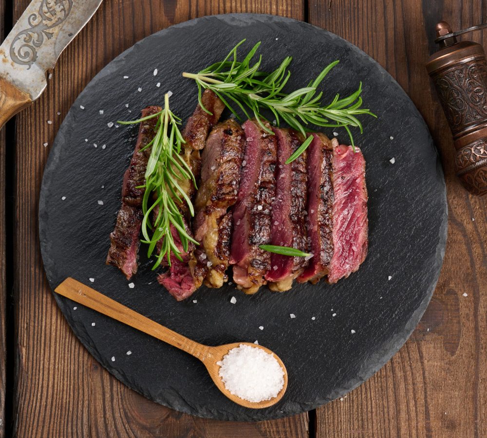 fried piece of beef ribeye cut into pieces on a black board, rare degree of doneness. Delicious steak, top view