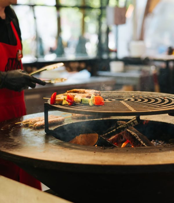 Unrecognizable chef cooking grilled vegetables and meat in an outdoor cafe. Close-up, selective focus on frying food