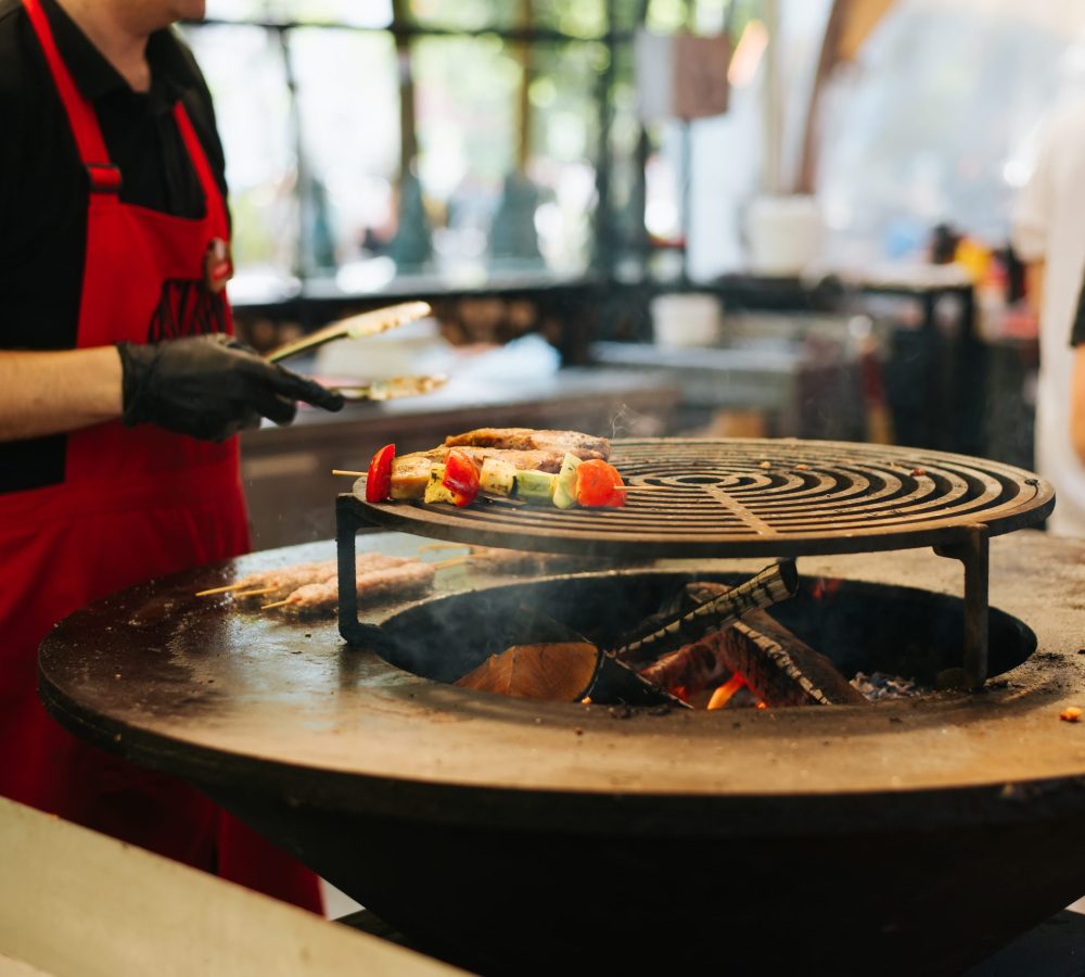 Unrecognizable chef cooking grilled vegetables and meat in an outdoor cafe. Close-up, selective focus on frying food